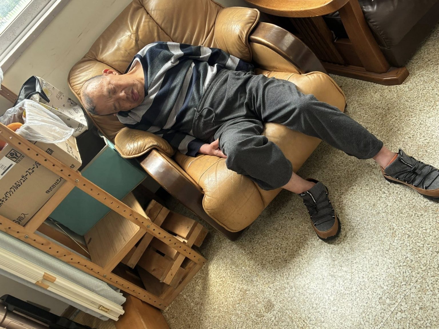 高齢者が共用部でくつろぐ様子。茶色い椅子でリラックスしている生活風景。